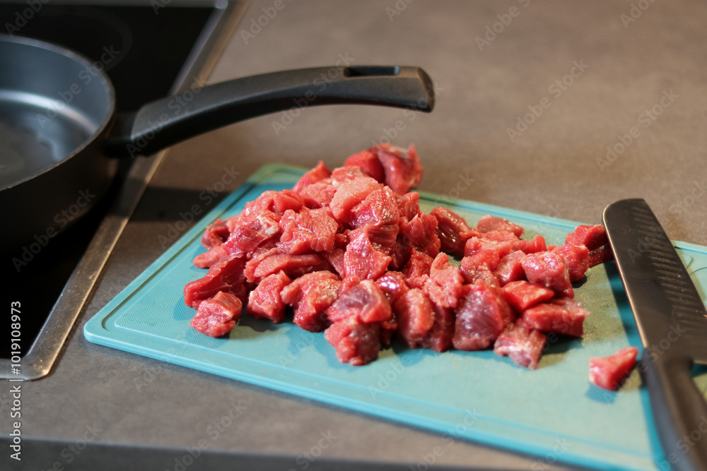 Close up of raw beef meat chopped in small cubes on green cutting board with a knife Close up of raw beef meat chopped in small cubes on green cutting board with a knife