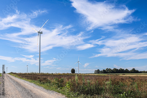 Wind turbines on a rural dirt road during sunny day with blue skies and wispy clouds in the background photo