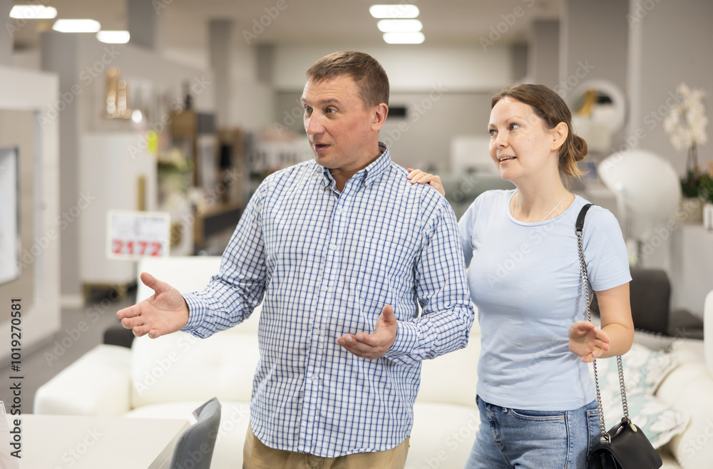 Fototapeta premium Couple in store inspects upholstered furniture. They runs hand over soft fabric, imagining how it would look in living room, and wonders if its worth investment.