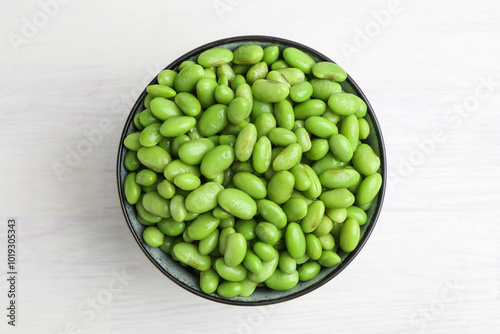 Fresh edamame soybeans in bowl on white wooden table, top view