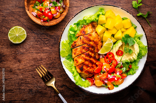 Foodie food salad bowl with grilled chicken and mango, tomato, cilantro, onion, salsa and lettuce wood background, top view photo