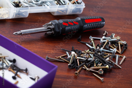 Different fasteners and crosstip screwdriver on wooden surface. Home repair concept