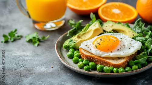 Nutritious breakfast plate with sunny-side-up egg on toast, avocado slices, green peas, and fresh orange juice. Healthy start to the day.