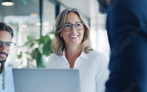 A woman smiles at colleagues in a modern office setting, showcasing collaboration and positivity in a professional environment. photo