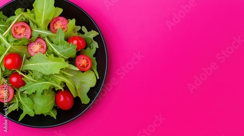 A vibrant fresh green salad featuring cherry tomatoes atop leafy greens, elegantly presented on a sleek black plate.