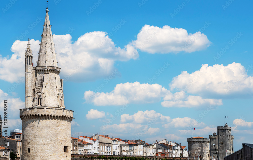Obraz premium city of La Rochelle with a tall tower and a cloudy sky. The sky is blue and the clouds are white