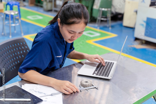 Asian woman technician engineer working designing mechanical parts engineering with laptop and checking an example small gear with metal ruler at industrial workshop.