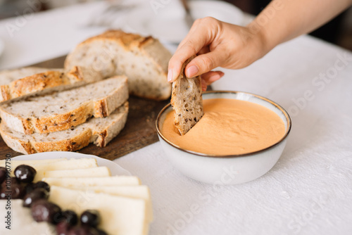 Hand dipping bread slice into creamy orange dip bowl. photo