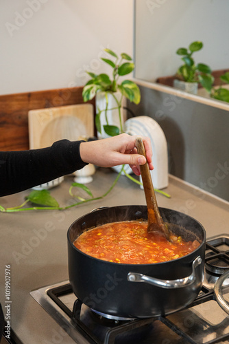 Person stirring a pot of tomato soup on the stove.
