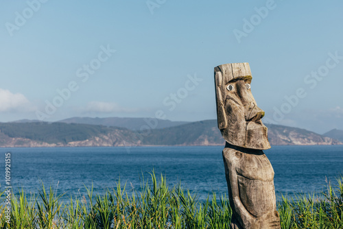 Wooden tribal sculpture overlooking serene coastline with mountains photo