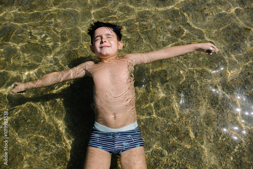 Young boy floating in clear water with relaxed expression photo