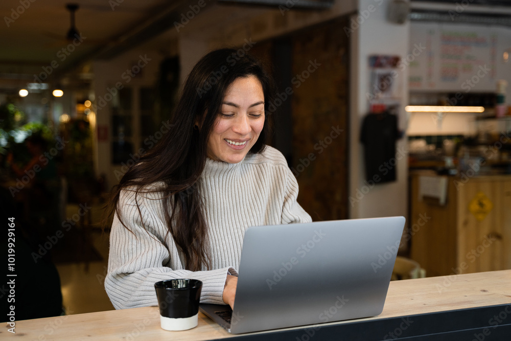 A woman smiling while using a computer at a coffee shop A woman smiling while using a computer at a coffee shop