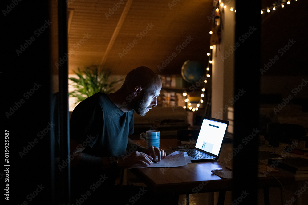 Man working late with laptop and papers Man working late with laptop and papers