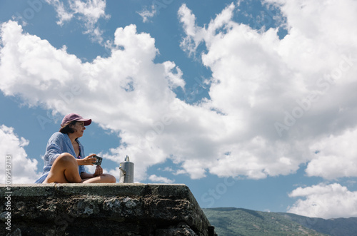 Woman relaxes holding a smartphone on stone dock under a cloudy sky photo