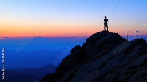 A lone figure stands on a mountain peak at sunset, silhouetted against the vibrant sky.