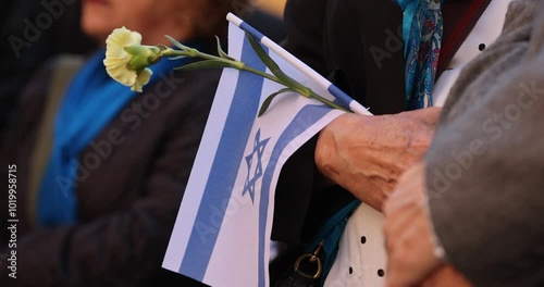 People hold the Israeli flag and flowers during a ceremony commemorating the October 2023 attacks on Israel.