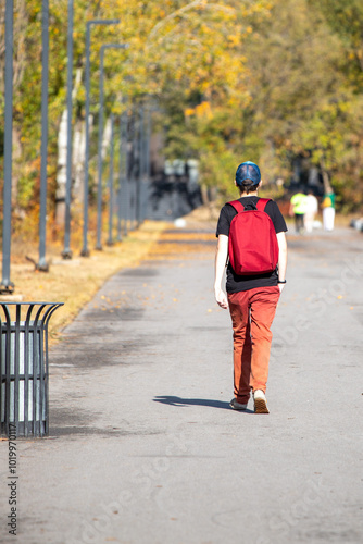 A young man wearing a red backpack walks down a sidewalk