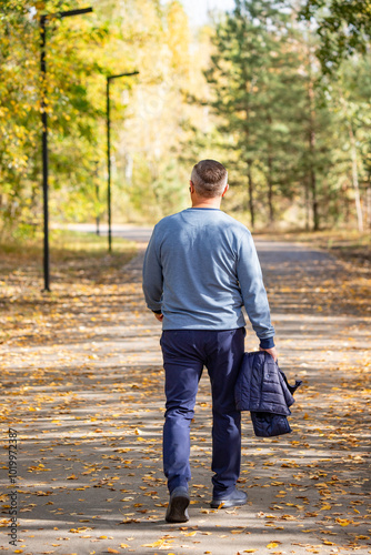 A man is walking down a path in the woods, wearing a blue sweater and blue pants