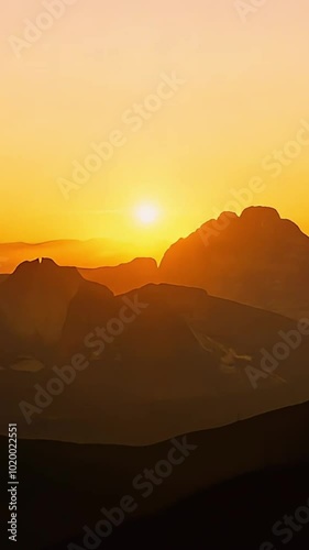 Silhouettes of mountains in a sunset with a bright sun in the sky.