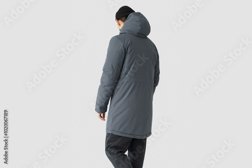 a man in a grey coat stands in front of a white background. Photograph of a man with his back turned photo