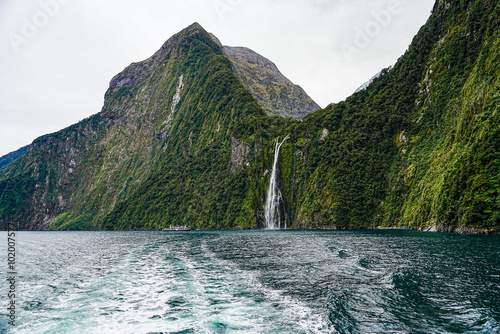 Breathtaking view of Milford Sound's fjords, waterfalls, and towering cliffs under a cloudy sky.