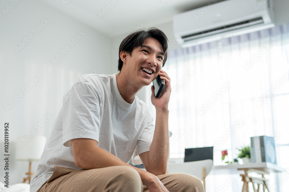 Asian young man talking on mobile phone call on bed at home in morning.