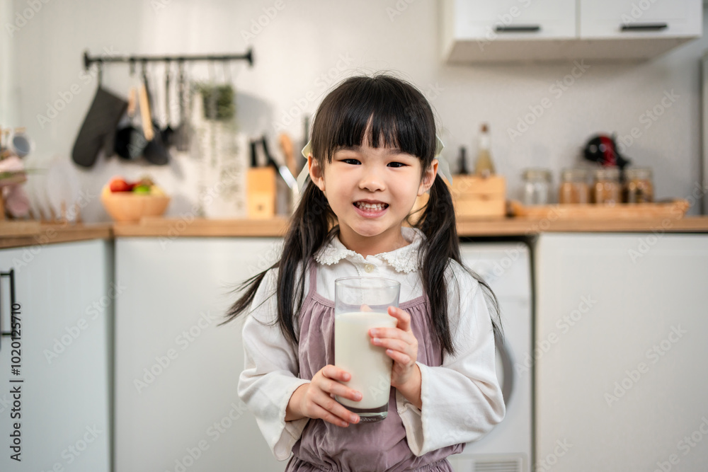 Portrait of Asian young girl drinking a glass of milk in kitchen at home.