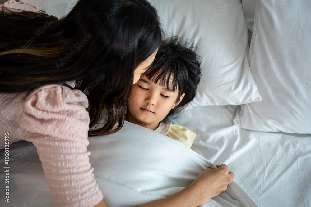 Asian loving mother take care of sleeping daughter in bedroom at home.