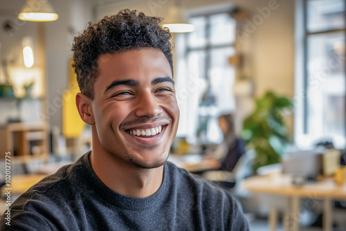 A smiling young man in a modern office setting with a relaxed atmosphere.