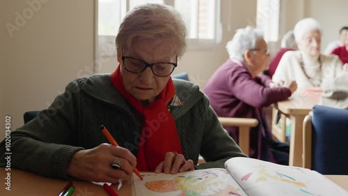 Elderly woman wearing a red scarf concentrates on drawing in her book, showcasing creativity and focus in slow motion