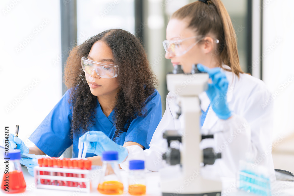 Two female scientists work in a laboratory with blood samples and test tubes filled with solution with pipettes from droppers while conducting research.