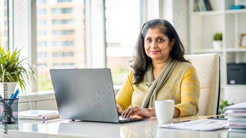 Cropped portrait of an middle aged India lady boss working on her computer while sitting in her luxury private office table , lot of file, check report project paper