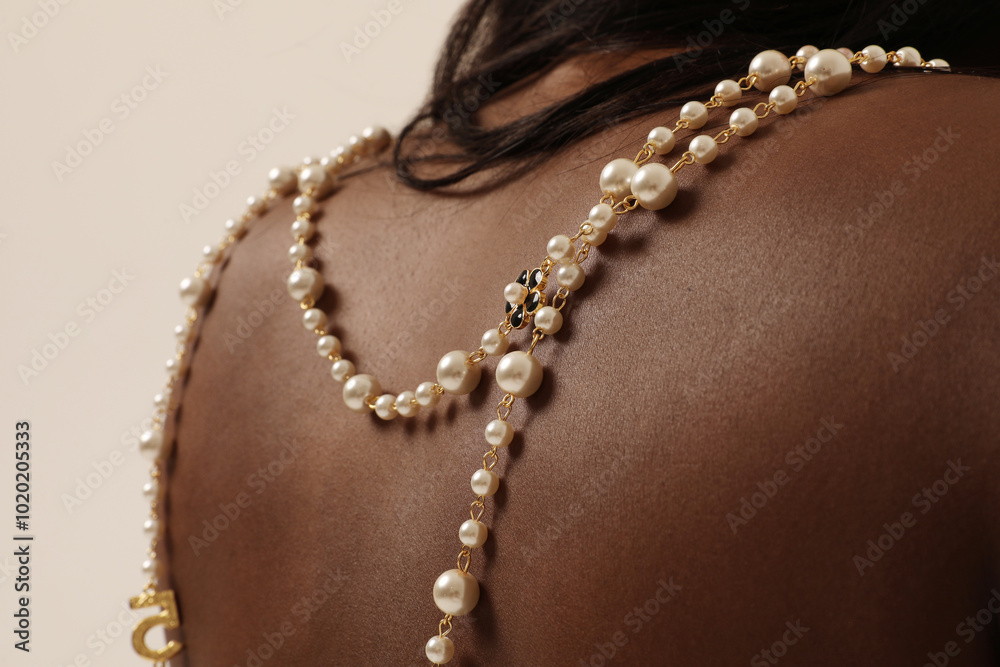 Dark-skinned young female model with pearl necklace on her shoulder posing over white wall. Dark-skinned young female model with pearl necklace on her shoulder posing over white wall.