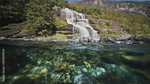 A split over-under view of the waterfall cascading into the fjord. Sun penetrates the water and dances on the rocky bottom. photo