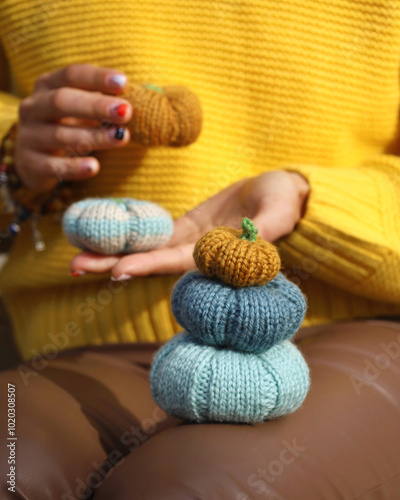 Obraz na płótnie Three colorful handmade knitting pumpkins in front and two others in woman's hands on background. Fall autumn concept. Person unrecognizable, wearing yellow sweater, brown leather pants. w salonie