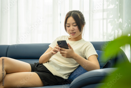 Image of young Asian girl using phone and relaxing at home