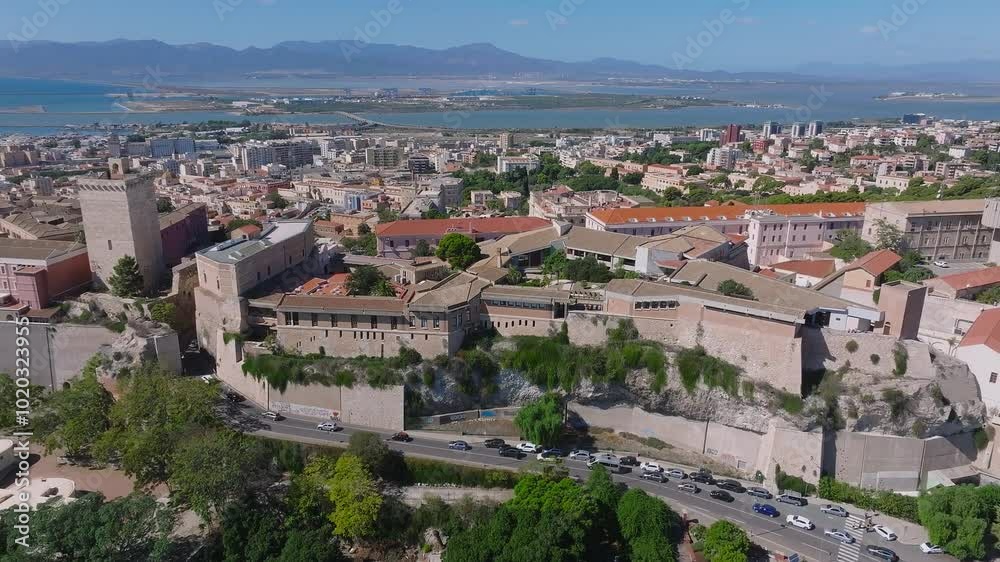 Cagliari's historic Castello district with terracotta roofs and fortifications, set against the Mediterranean Sea's azure waters, is seen from above.