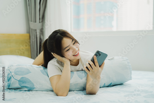 Image of young Asian girl using phone and relaxing in bed