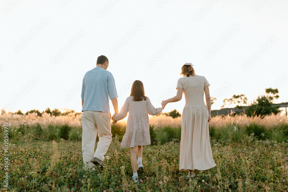 Happy family with child holding hands of each other and running through wheat field at sunset enjoying nature together Happy family with child holding hands of each other and running through wheat field at sunset enjoying nature together