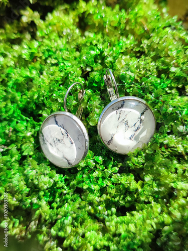 Handmade resin round marble texture stone earrings transparent finish at green moss background close. Leverback hooks, secure wear, nature-inspired jewelry, handcrafted silver jewellery, accessory, be photo