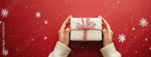 Paquete regalo envuelto en papel regalo blanco y lazo rosa, siendo colocado con las manos, sobre superficie roja decorada con estrellas en color blanco