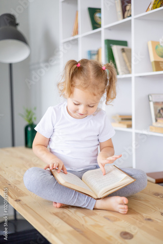 a small blonde girl reads books in a bright library at home, education and science for children