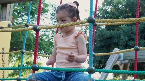 A young child with disability plays at a colorful jungle gym at the park, surrounded by trees. Hand held shot, 4K footage. photo