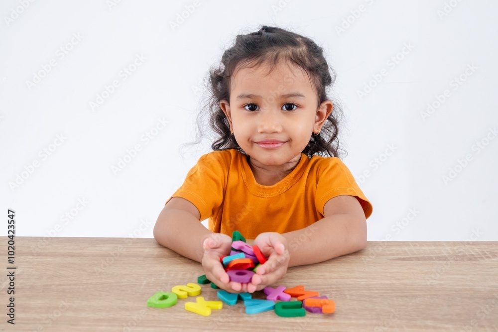 A happy little girl sitting at table with handful of wooden alphabet letters in palm A happy little girl sitting at table with handful of wooden alphabet letters in palm