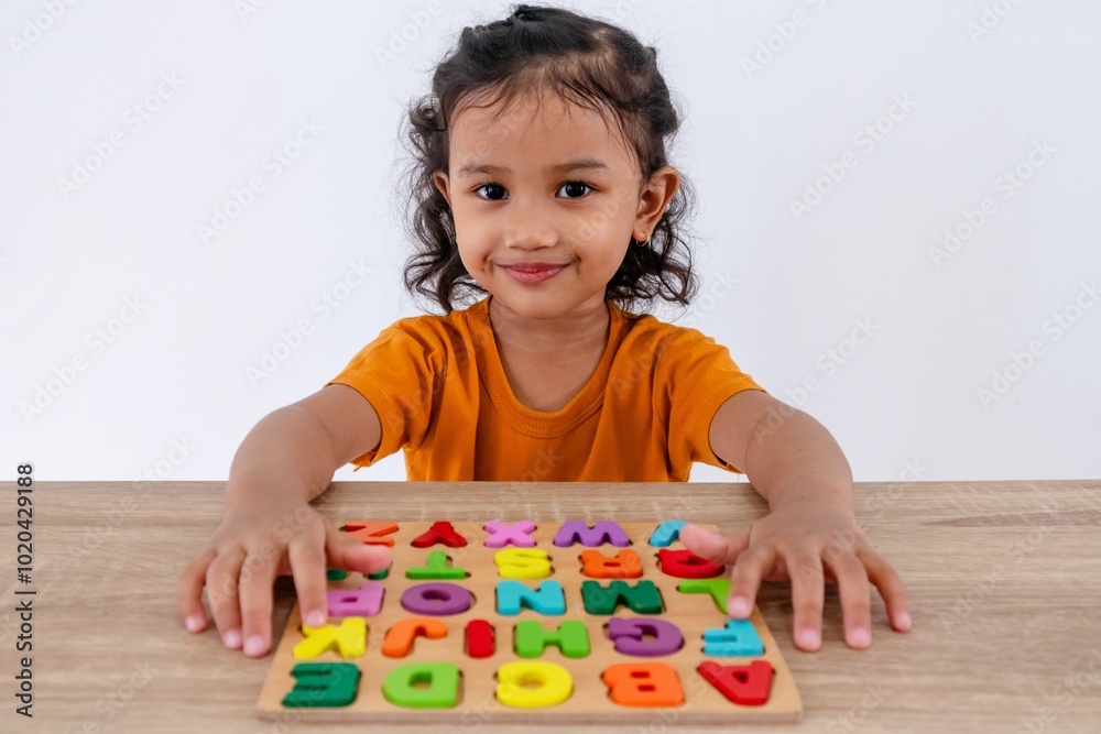 A cheerful little Asian girl plays with wooden alphabet letters on a table A cheerful little Asian girl plays with wooden alphabet letters on a table