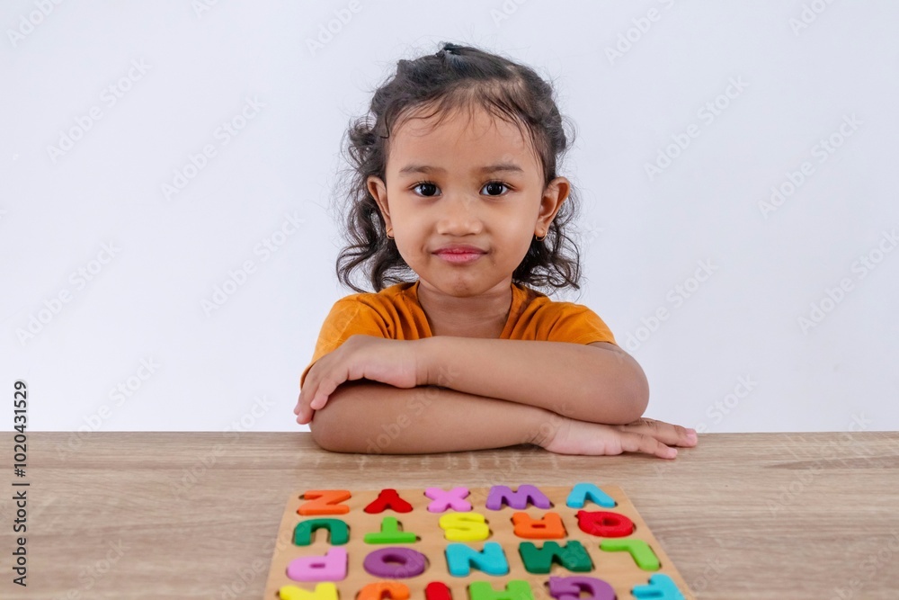 Asian little girl crossing her arms on the table with wooden alphabet letters for playing and learning Asian little girl crossing her arms on the table with wooden alphabet letters for playing and learning