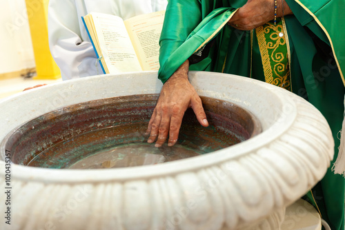 Fotografie Priest blessing water of baptismal font in church ceremony