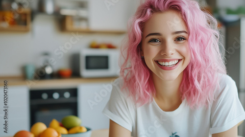 A dynamic young woman with pink hair, smiling brightly as she interacts with her colleagues on a video call. SheÃ¢ÂÂs seated at a stylish kitchen table, with colorful fruit bowls and photo