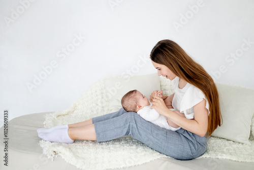 mom holds a small newborn baby girl at home on a white sofa and kisses him. Maternal love and care, space for text