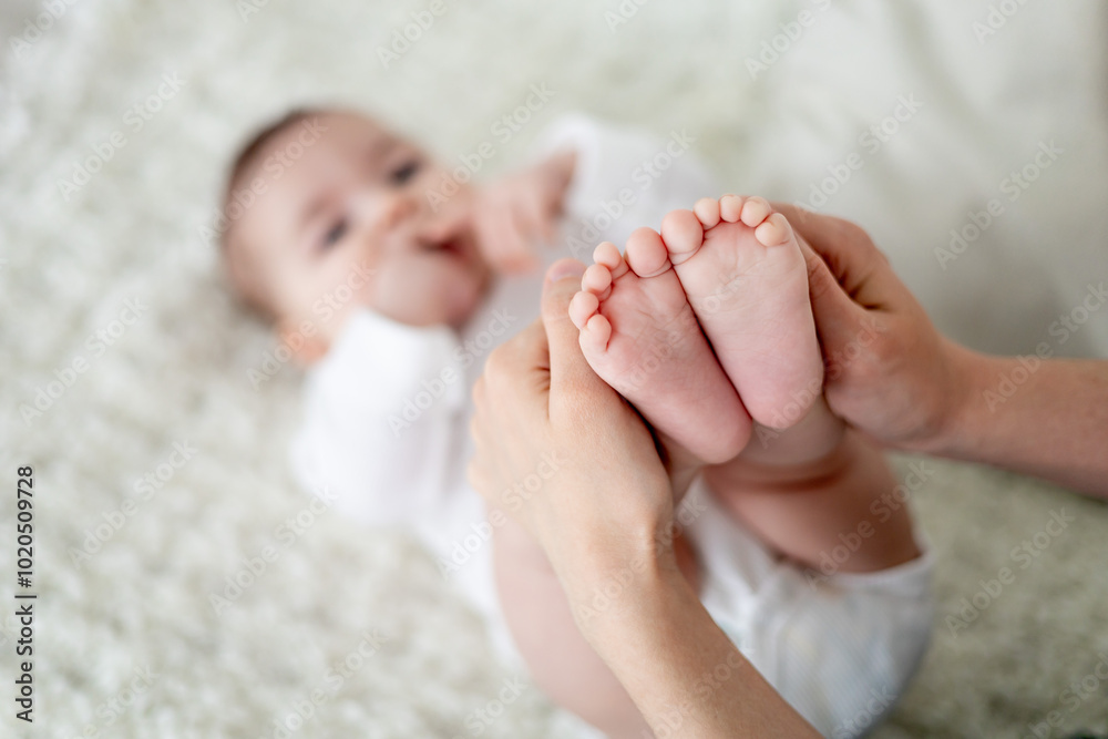 mom's hands hold the little nights of a newborn baby on a white sofa. Maternal love and care. Baby's heels in focus mom's hands hold the little nights of a newborn baby on a white sofa. Maternal love and care. Baby's heels in focus